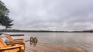A wooden dock with chairs and a metal railing extending into a calm lake, surrounded by trees. - Crystal Palace Cottage, Kawartha Lakes (Kinmount)