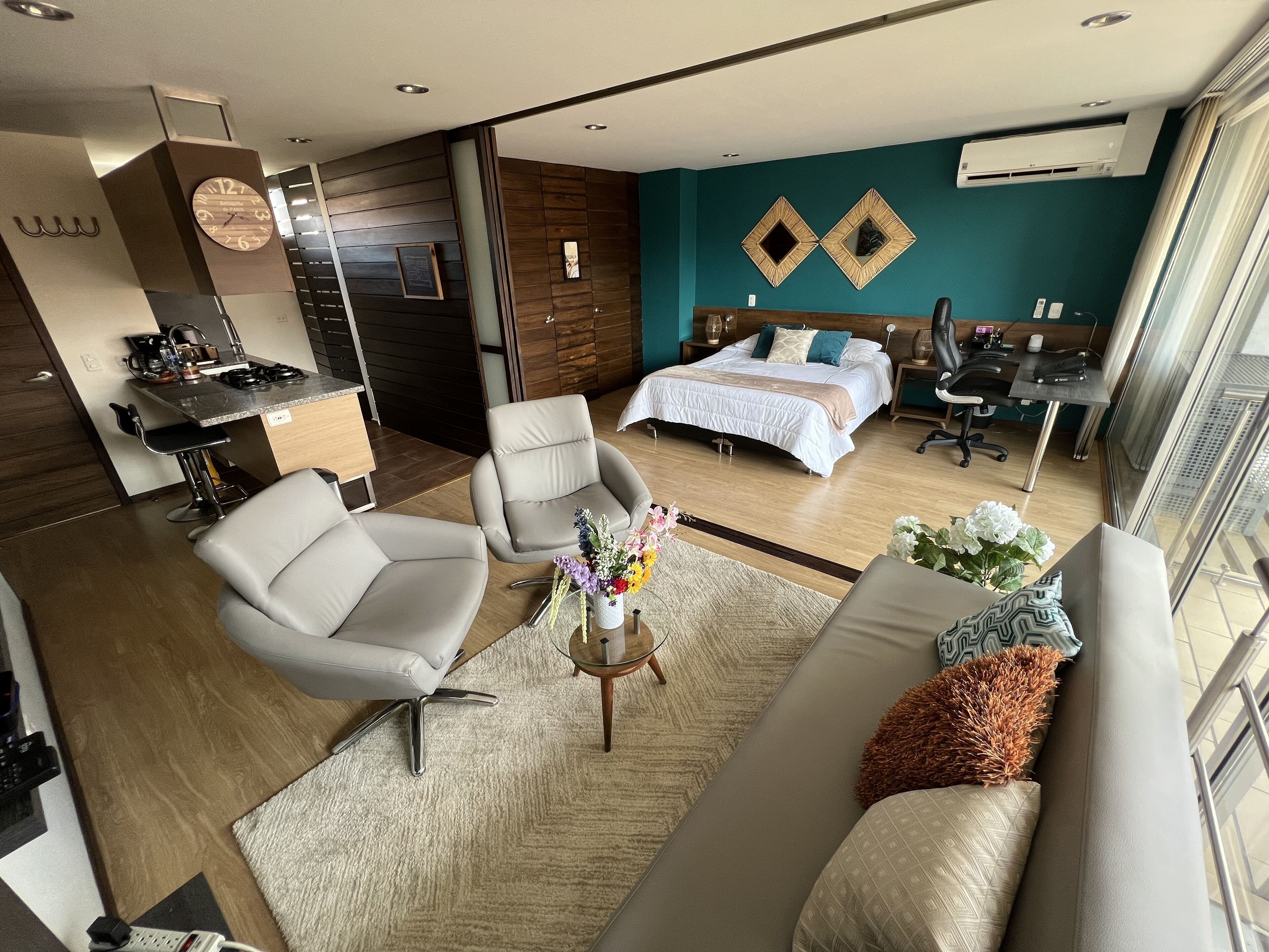 A modern hotel room with a bed, two armchairs, a sofa, a small dining area, and a view of the city.