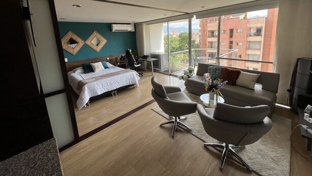 A modern hotel room with a large bed, a desk, a sofa, and a balcony with a city view.