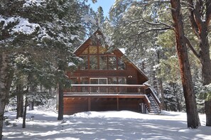 A cabin with a wooden exterior, a balcony, and a staircase leading to the entrance.