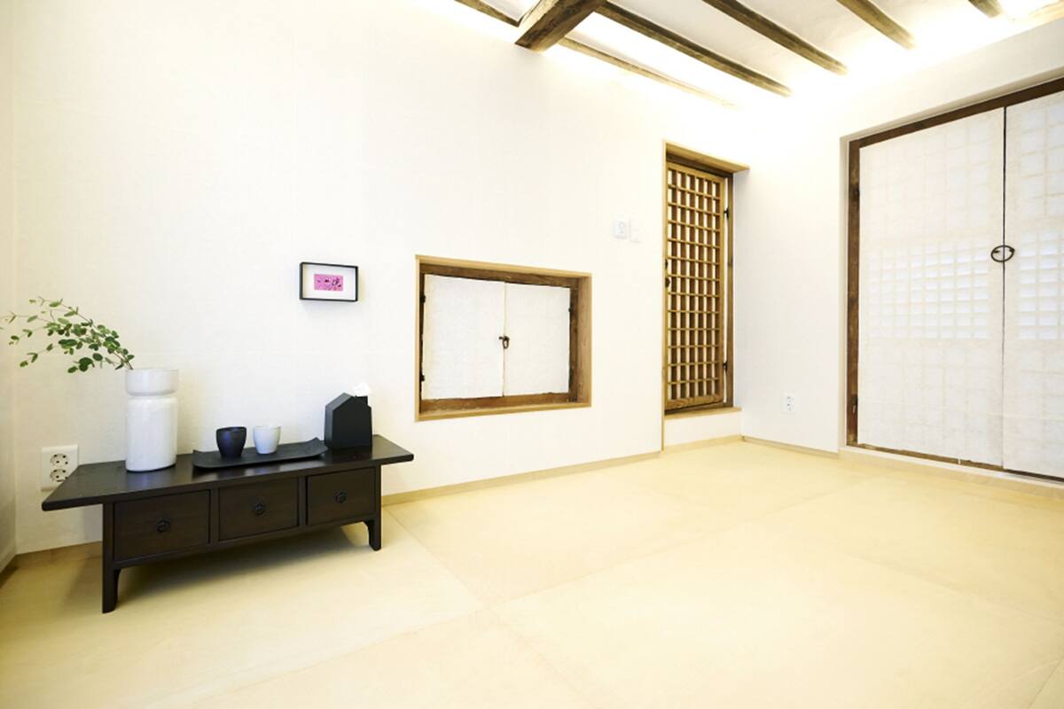 A minimalist room with a tatami mat floor, a dark wooden bench, a shoji screen, and a traditional Japanese sliding door.