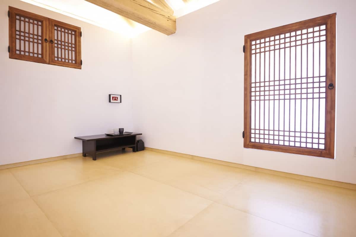 A room with a low wooden bench, a small table, and a large window with a grid pattern.