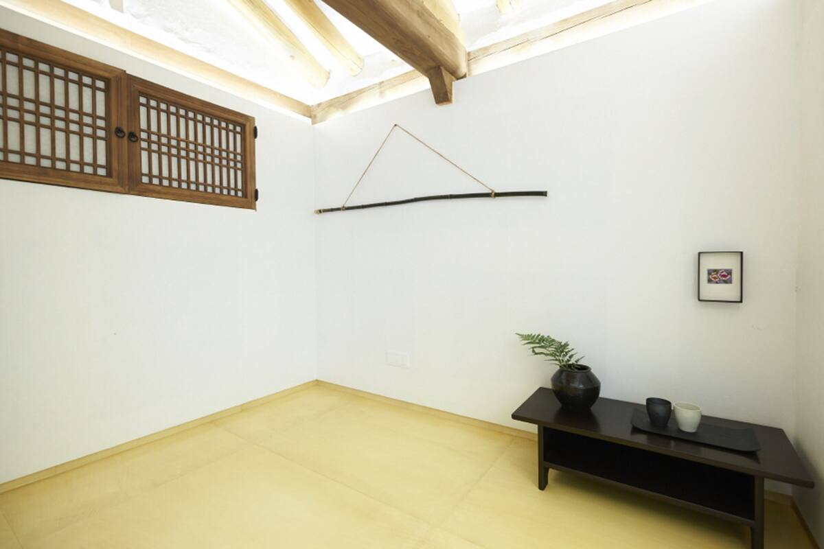 A room with a wooden ceiling, a black bench, a potted plant, and a framed picture on the wall.