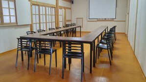 Een vergaderruimte met een lange tafel en stoelen, houten balken in het plafond en een projectiescherm aan de muur.