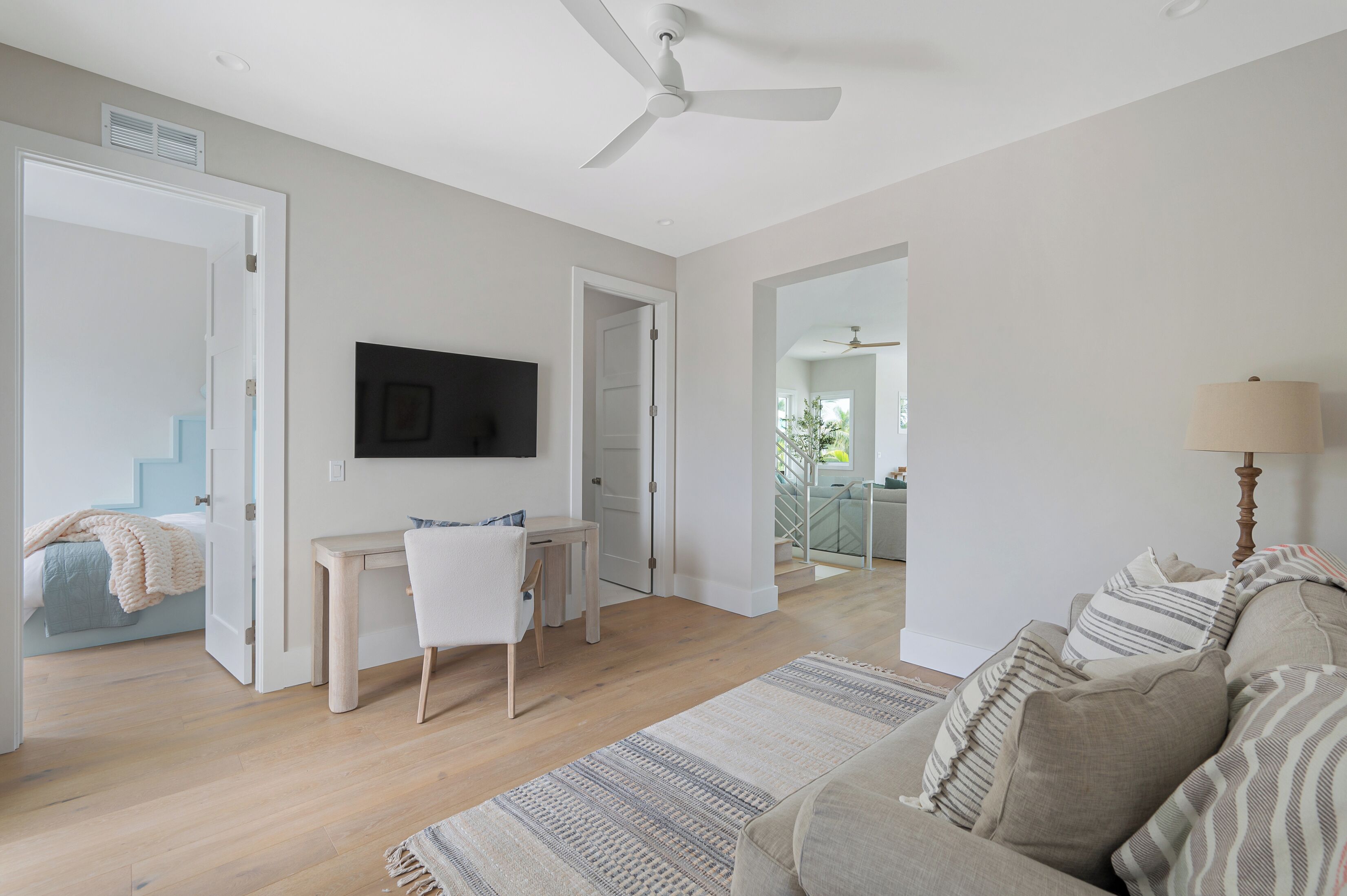 A spacious living room with a large window, a ceiling fan, a TV mounted on the wall, and a cozy seating area with a sofa and a coffee table.