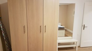 Un dormitorio con un amplio armario de madera, un banco blanco y una puerta.
