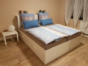 Ein Bett mit gemustertem Bettbezug, zwei Kissen und ein Nachttisch mit Lampe.