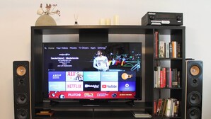 Un televisor sobre un mueble multimedia negro con un estante de libros y dos altavoces.