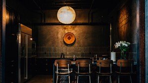 A restaurant with a bar area, wooden chairs, a round table, and a hanging light fixture. - Native Hostel Austin (Austin)