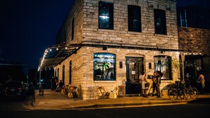 A stone building with a large window and a door, outdoor seating, and bicycles. - Native Hostel Austin (Austin)