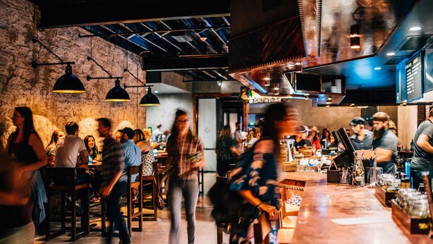 A busy bar with patrons and staff, exposed brick walls, and hanging pendant lights. - Native Hostel Austin (Austin)