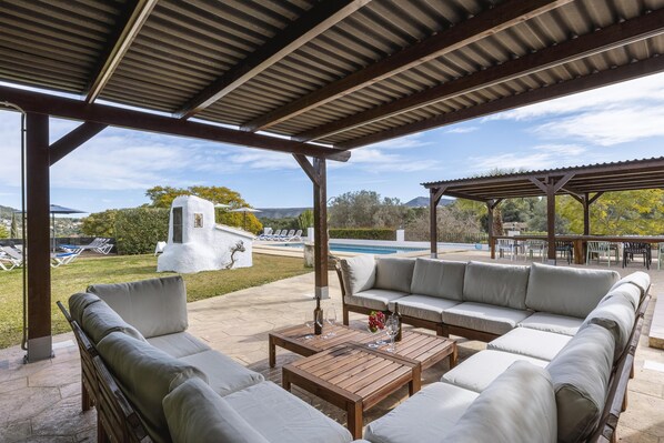 A covered outdoor seating area with a pool in the background.
