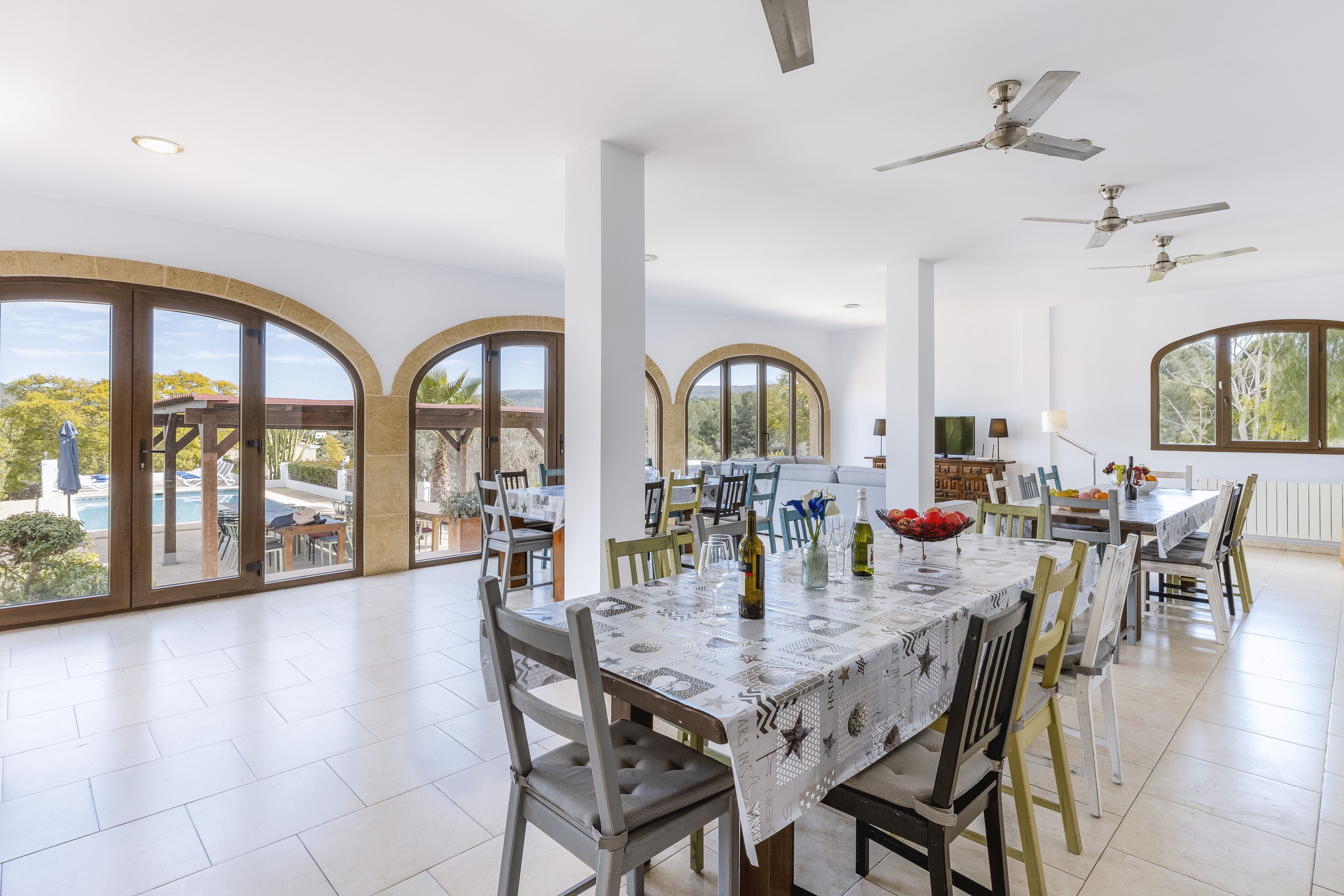 Uma sala de jantar ampla, com uma mesa grande, várias cadeiras e vista para o exterior através de janelas em arco.