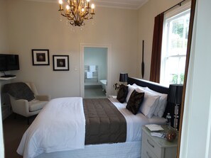 A hotel room with a bed, a chair, a TV, a chandelier, and a bathroom visible through an open door. - Andelin Guest House (Auckland)