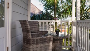 A covered porch with wicker furniture and a glass table, surrounded by white railings and palm trees. - Andelin Guest House (Auckland)