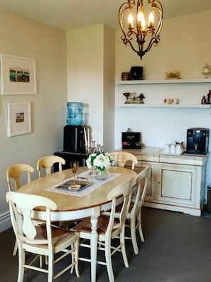 A dining area with a round table, chairs, and a chandelier. There are shelves above the table with various items. - Andelin Guest House (Auckland)