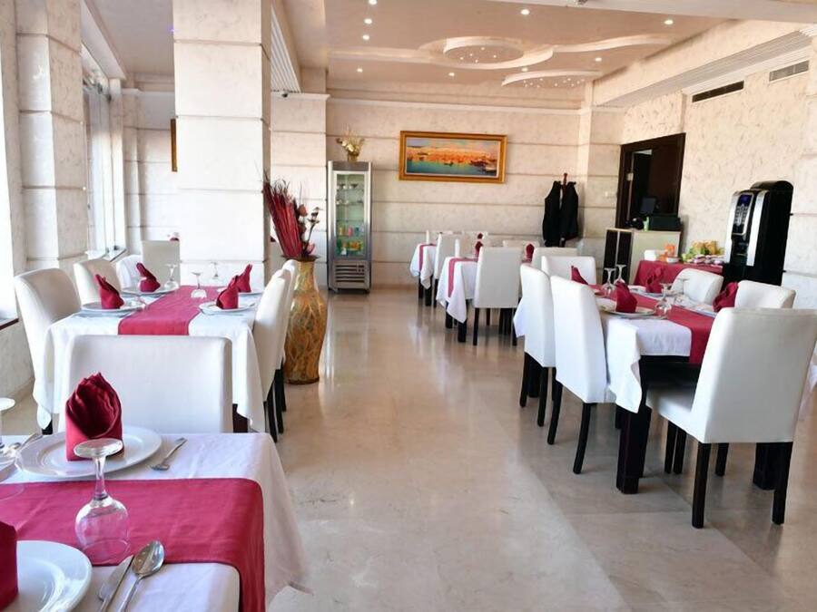 A dining area with white tables and chairs, red napkins, and a painting on the wall.