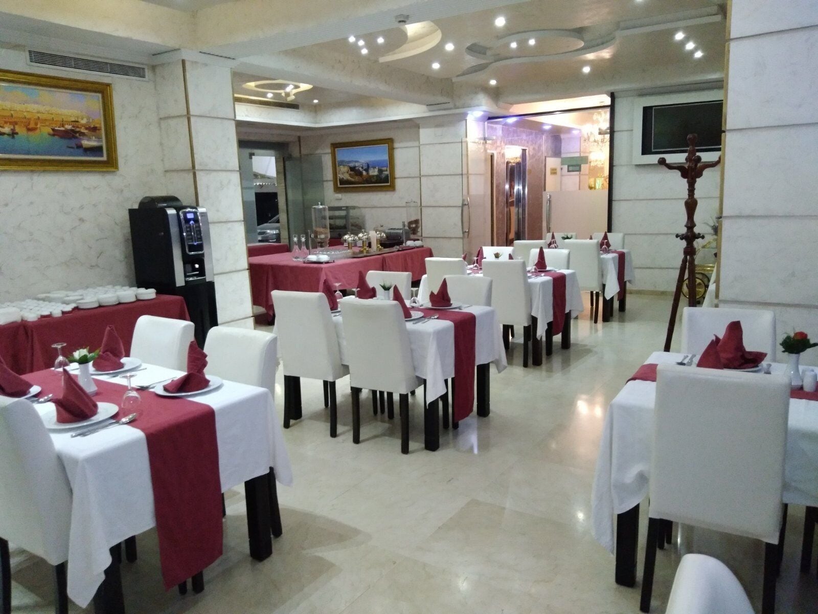 Un restaurante con varias mesas dispuestas para comer, un cuadro grande en la pared y un dispensador de agua.