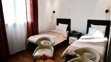 Una habitación de hotel con dos camas, una mesita con un jarrón de flores y una silla.