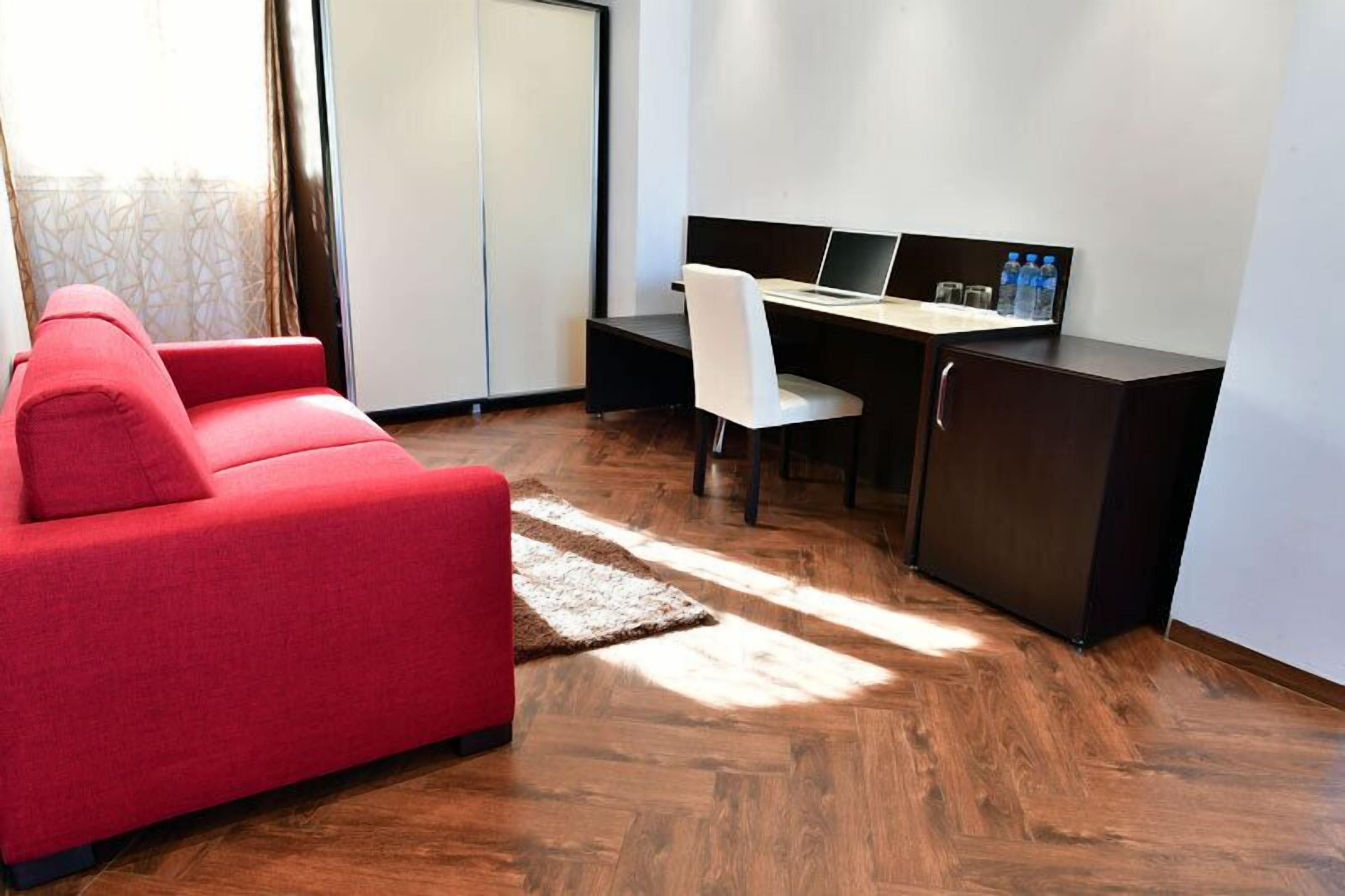 A modern room with a red sofa, a desk with a laptop, and a cabinet.
