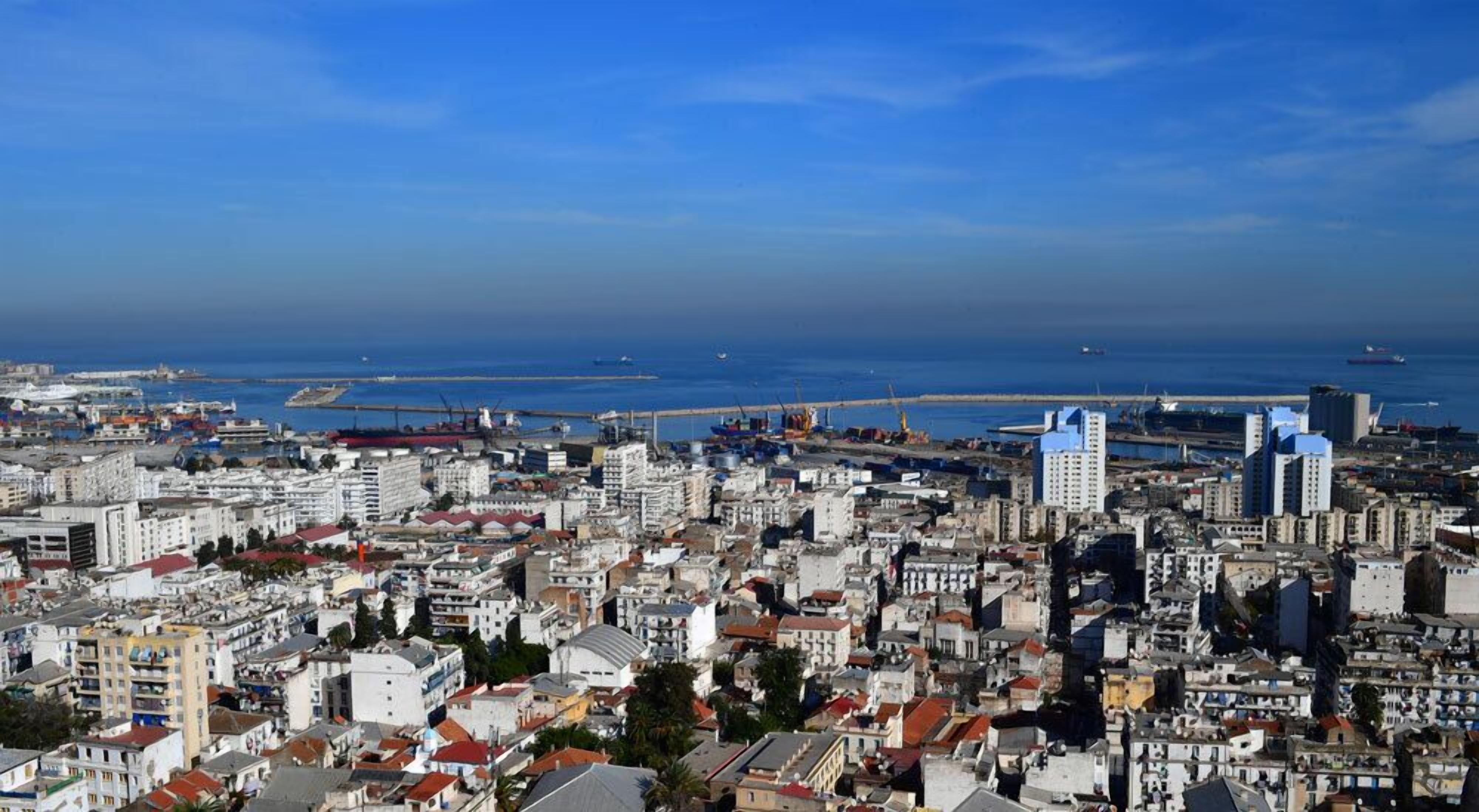 A coastal cityscape with dense urban buildings, a marina, and a clear blue sky.