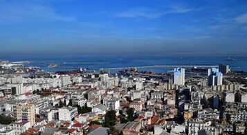Un paisaje urbano costero con edificios densos, un puerto deportivo y un cielo azul despejado.
