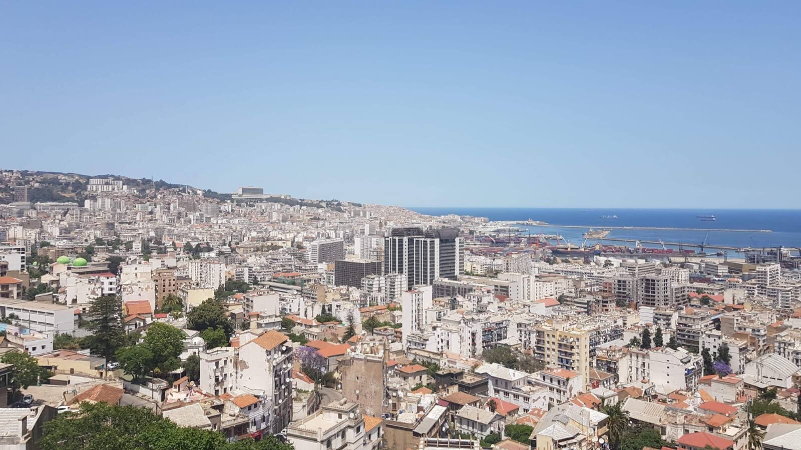 Un paisaje urbano con edificios densos, un cielo azul despejado y una vista distante del mar.