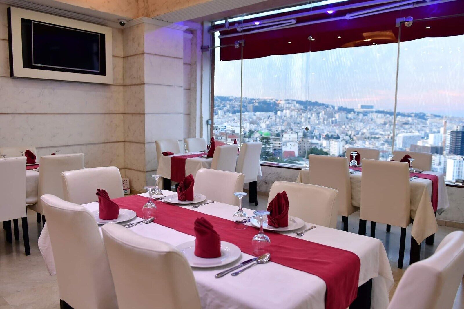 Un restaurante con mesas dispuestas para comer, vistas a la ciudad y un televisor en la pared.