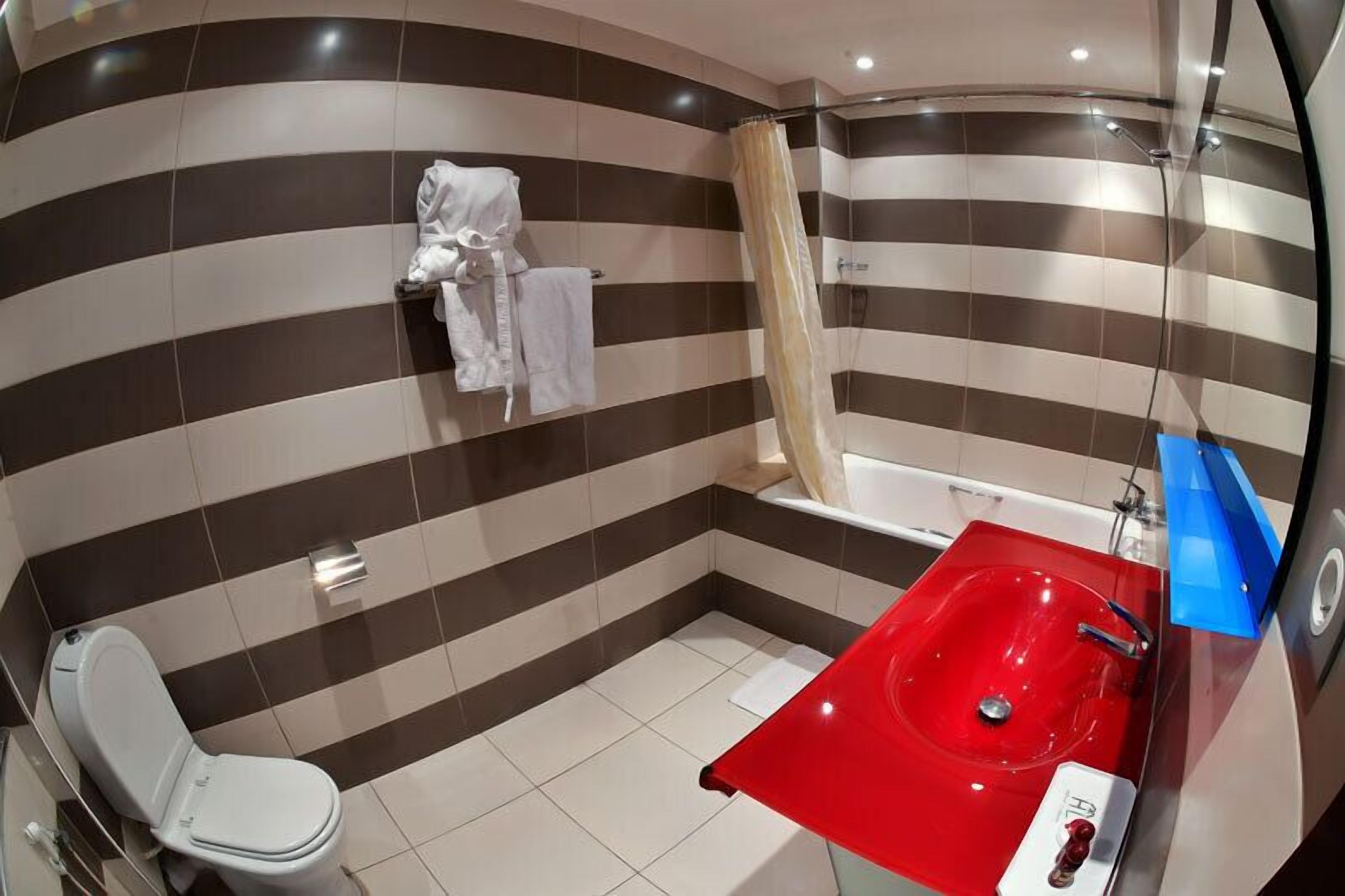 A bathroom with striped walls, a white toilet, a red sink, and a shower curtain.