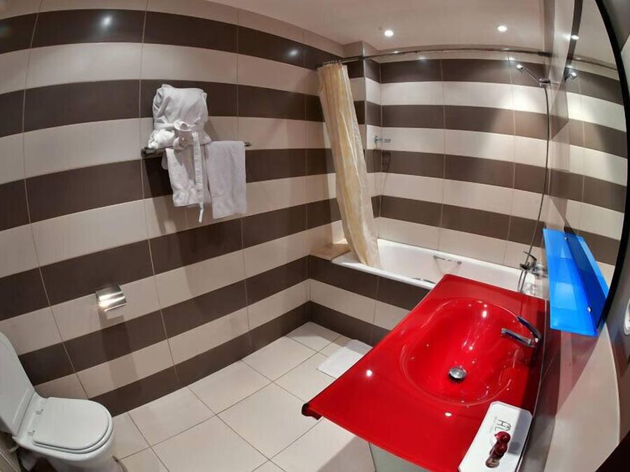 Un baño con paredes a rayas, un inodoro blanco, un lavamanos rojo y una cortina de ducha.