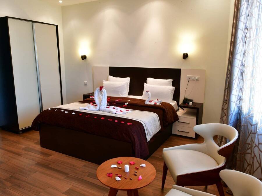 Habitación de hotel con cama, dos mesitas de noche, una silla, una mesita con pétalos de rosa y un armario.