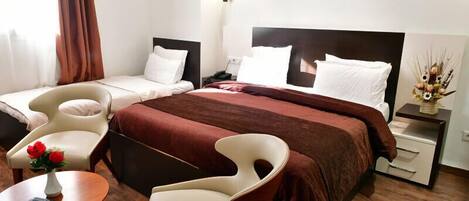 Habitación de hotel con cama, dos sillas, una mesita con un jarrón de flores y una mesita de noche con lámpara.