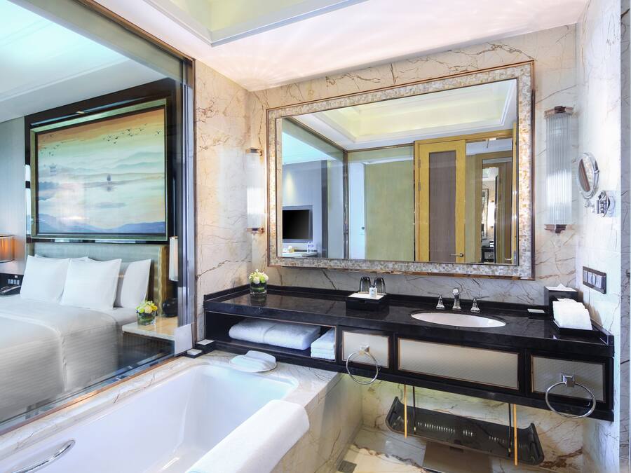 A modern hotel bathroom with a large bathtub, a double sink vanity, and a large mirror.