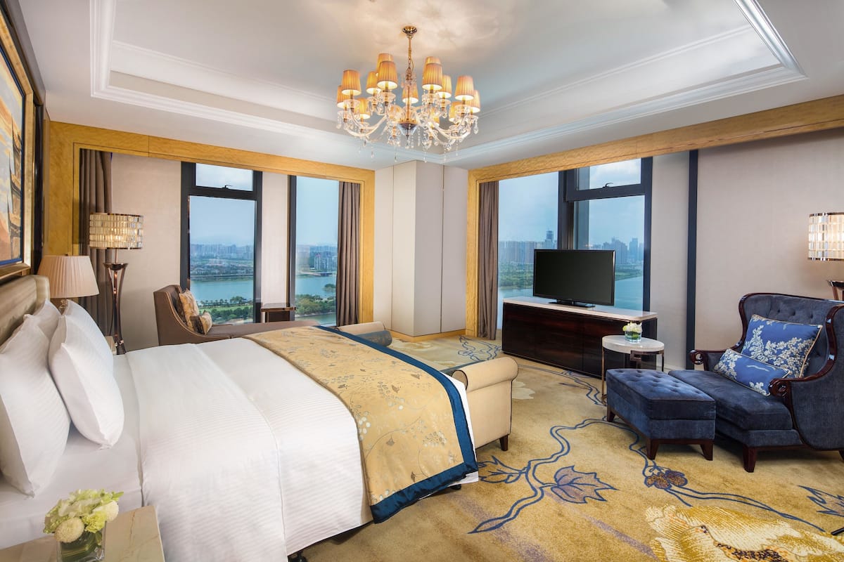 A hotel room with a large bed, a sofa, a TV, and a view of a cityscape.