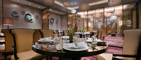A dining area with round tables, chairs, and hanging chandeliers.