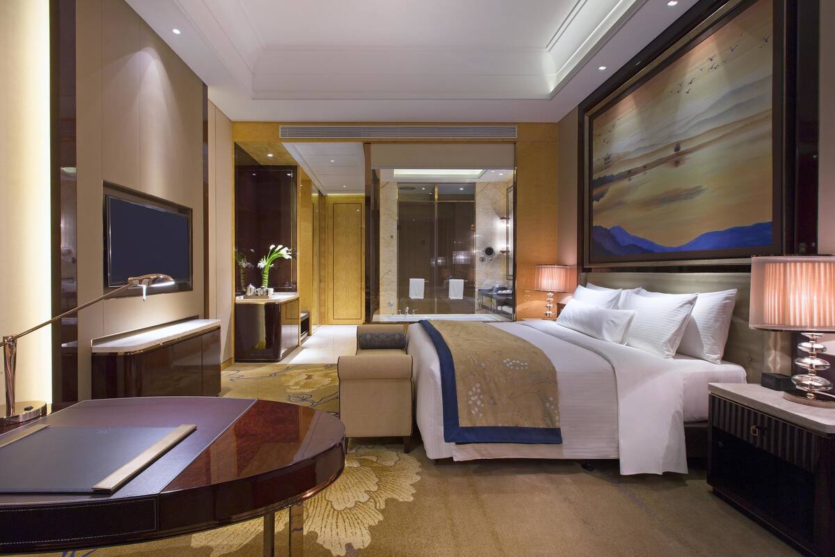 A hotel room with a bed, bedside table, lamp, and a large painting on the wall.
