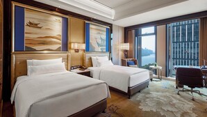 Habitación de hotel con dos camas, un escritorio, una silla y grandes ventanales con vista a la ciudad.
