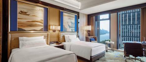 A hotel room with two beds, a desk, a chair, and large windows with a city view.