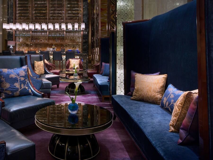 A luxurious lounge area with plush seating, a bar with shelves of bottles, and a decorative wall.