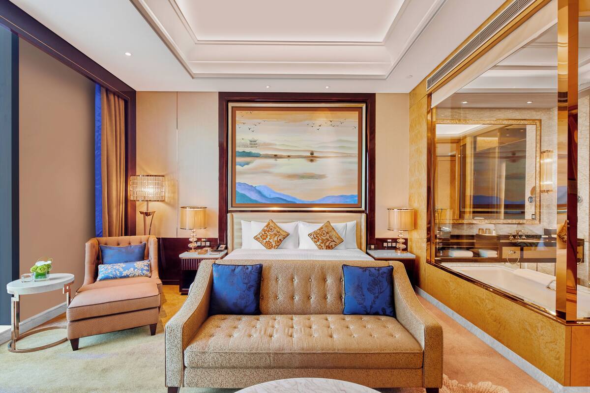 A hotel room with a large bed, a sofa, a chair, a round table, and a large mirror.