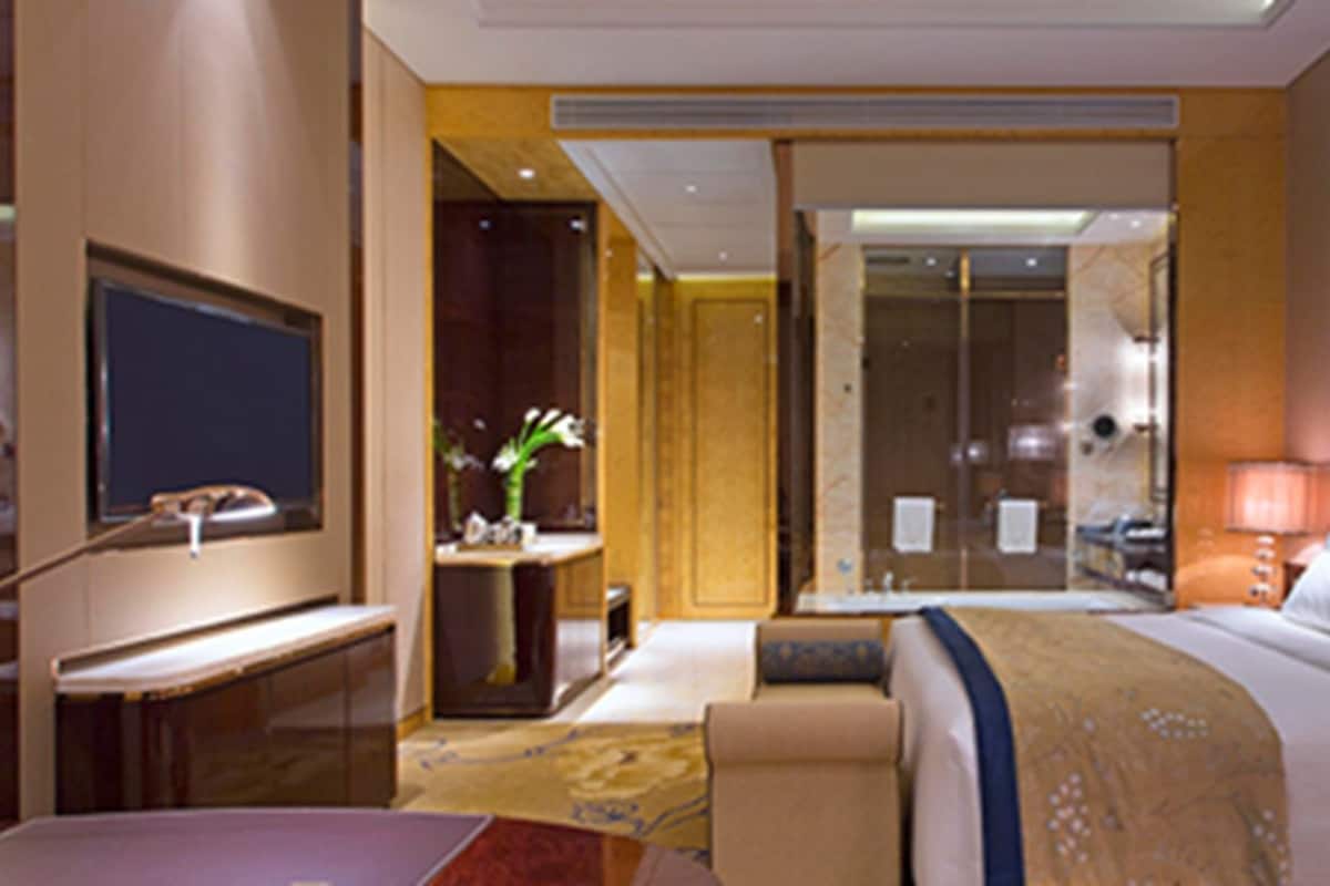 Une chambre d’hôtel avec un lit, un bureau, une télévision, une salle de bain et un tableau au mur.