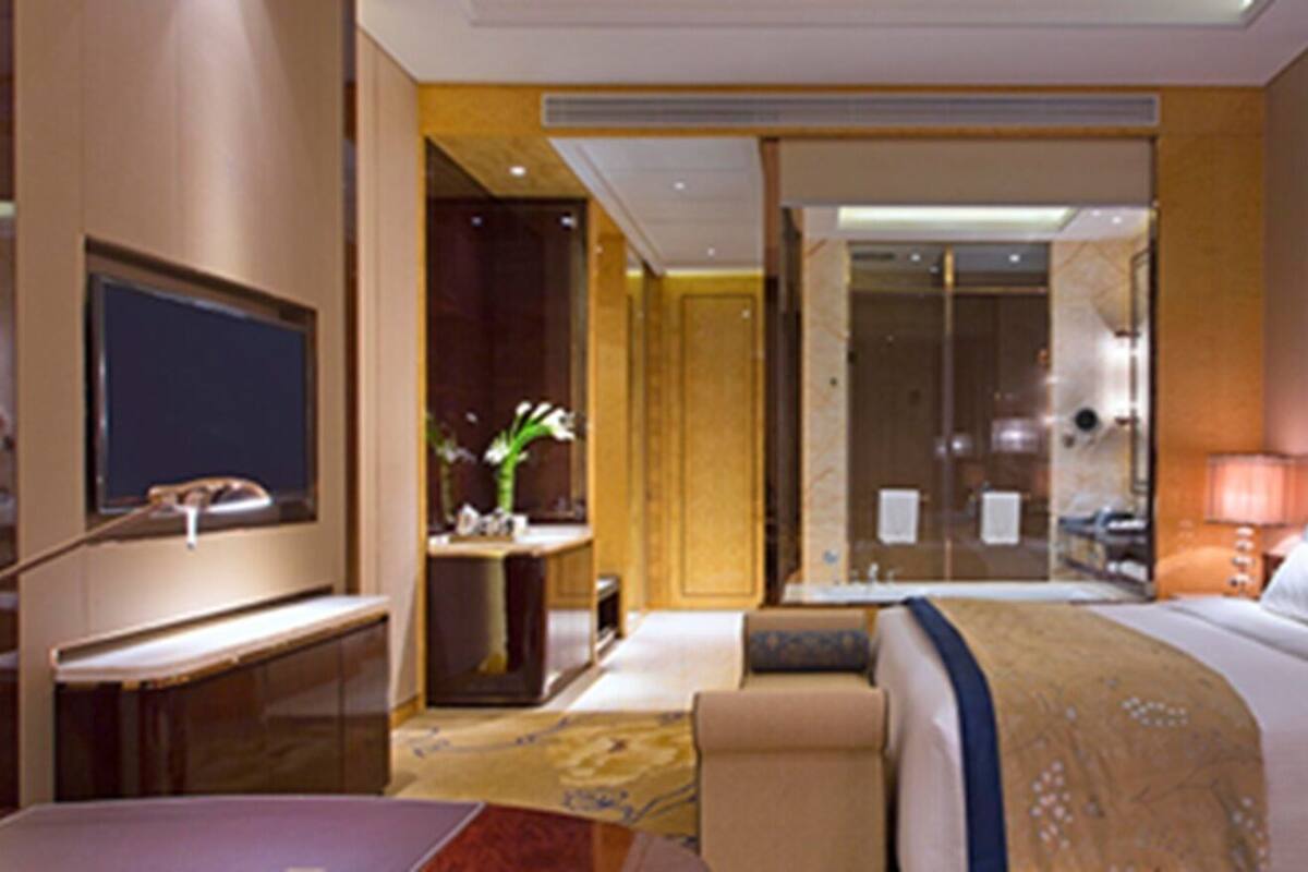 A hotel room with a bed, a desk, a TV, a bathroom, and a painting on the wall.