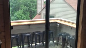 A room with a sliding glass door leading to an outdoor area with a wooden deck and black plastic stools. - Ultra-hip, Family-Friendly, Modern Space- SKI IN SKI OUT! (Champion)