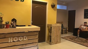 A reception area with a wooden counter labeled "HOOD," a brown door, and a wall-mounted plant. - HOOD - Hostel (Kota Kinabalu)