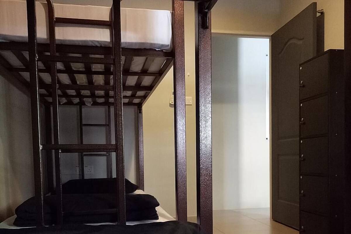 Un lit superposé avec une échelle, un matelas noir et une couverture à carreaux. La pièce contient une porte avec une poignée et une armoire de couleur sombre.