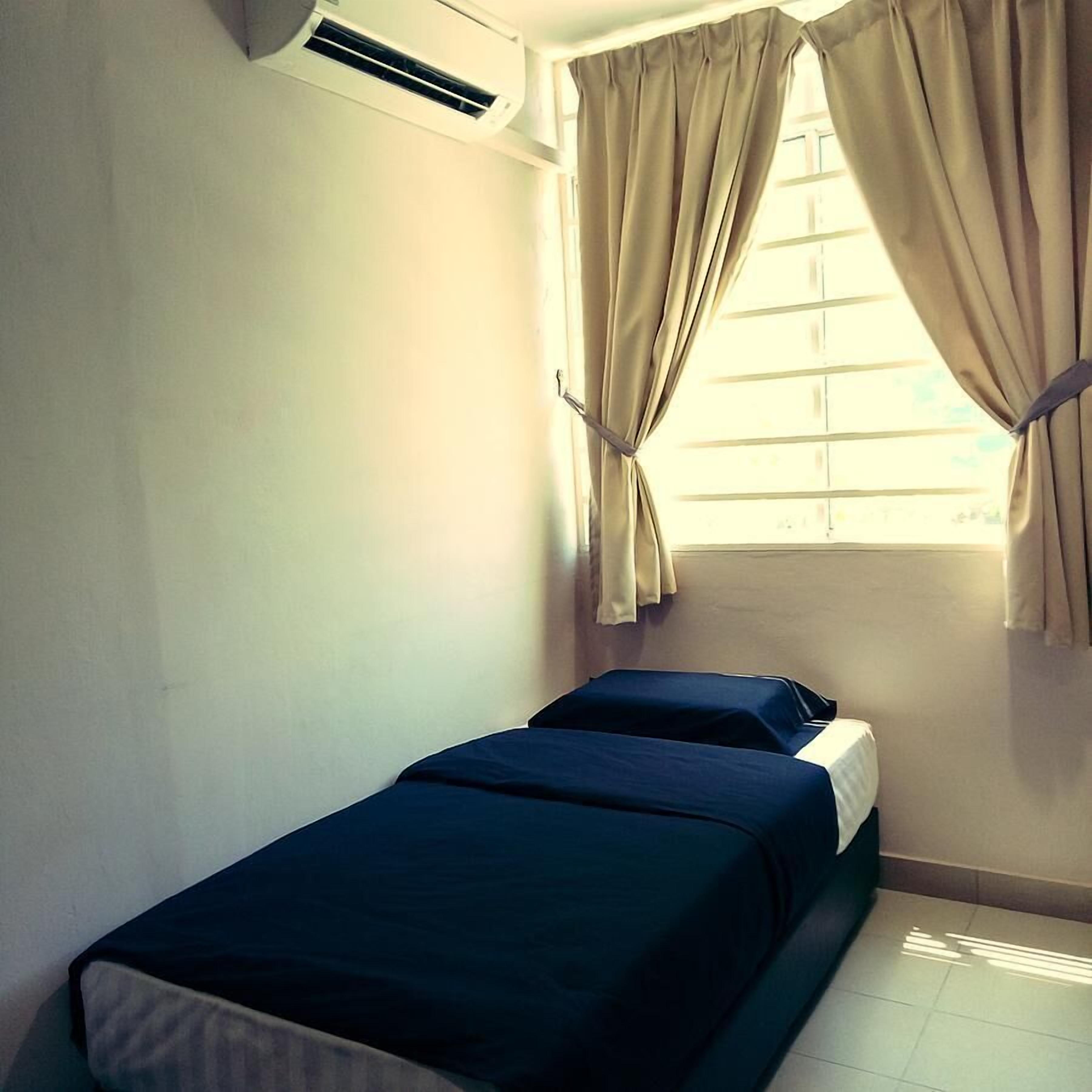 A small, single-bed room with a window, curtains, and an air conditioning unit.