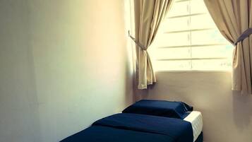 A small, single-bed room with a window, curtains, and an air conditioning unit.
