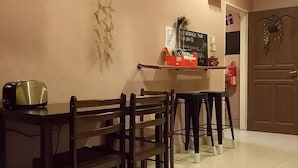 A dining area with a wooden table and chairs, a small kitchen area with a kettle, and a chalkboard menu. - HOOD - Hostel (Kota Kinabalu)