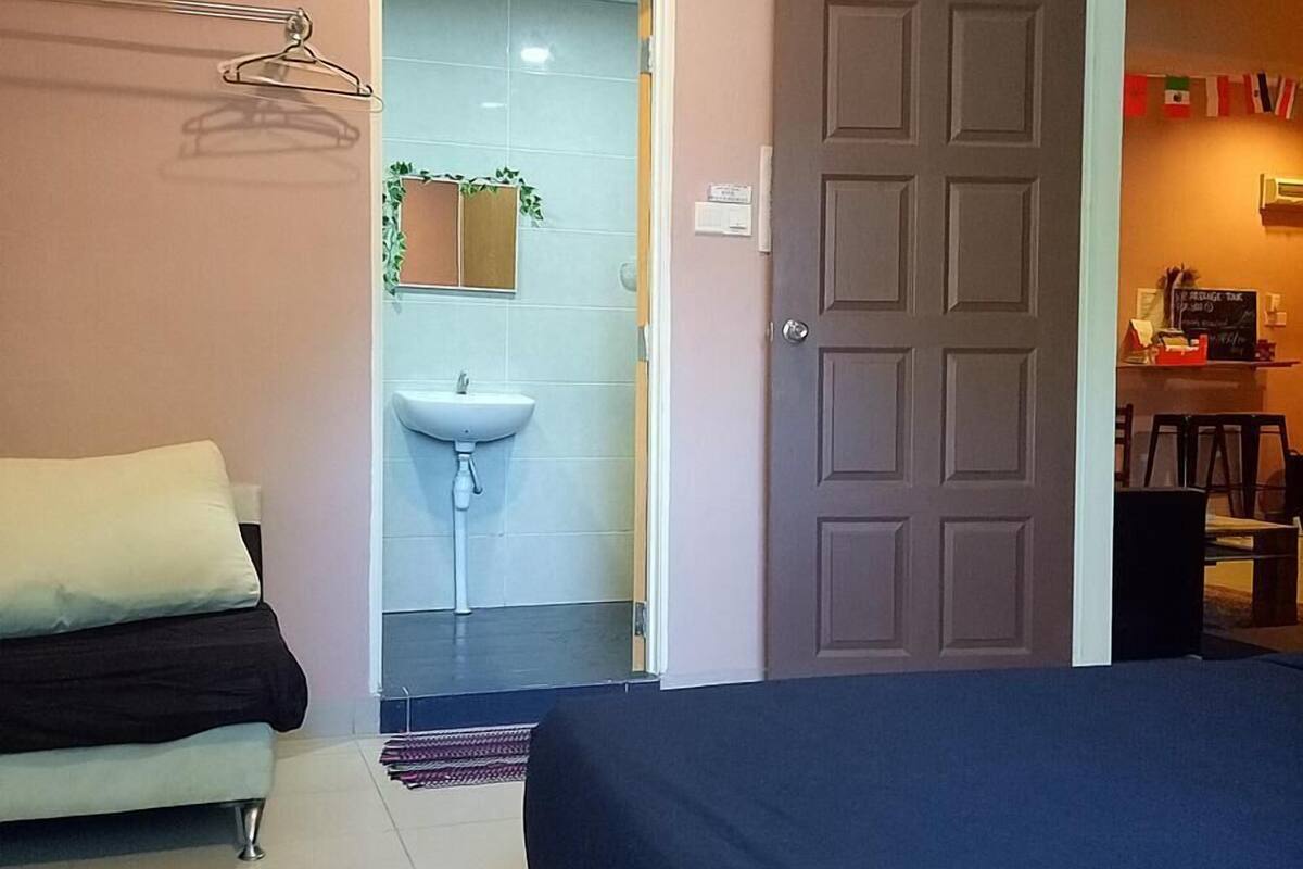 Une chambre à coucher comprenant un lit, une table de chevet, une lampe suspendue, une porte donnant sur une salle de bain et un petit bureau avec une chaise.