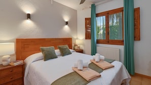 A well-lit bedroom with a wooden headboard, two wall-mounted lights, a window with curtains, and neatly arranged towels on the bed. - Casa Virginia 6 pax - Javea, Costa Blanca (Javea)
